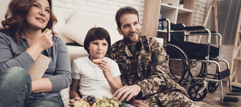 Veteran watching tv with family on ground at home.