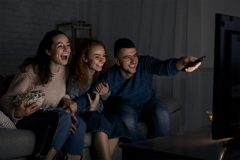 Excited friends watching TV and switching channels in the dark.