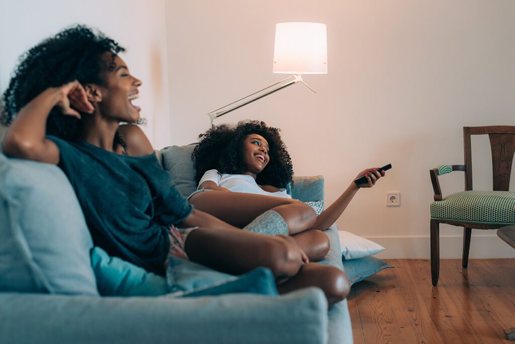 Happy women lying down in the couch watching tv.