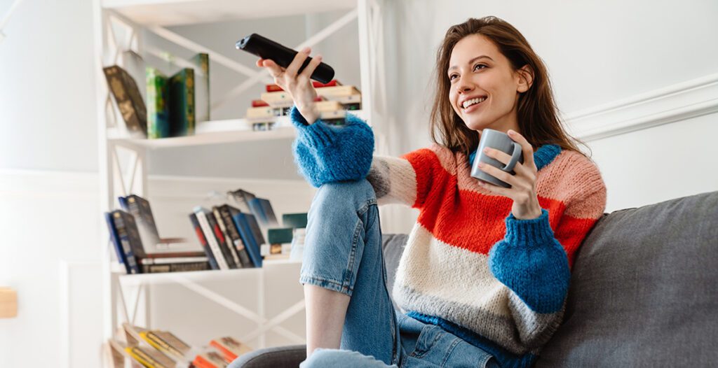 Girl drinking coffee and using remote control watching tv.